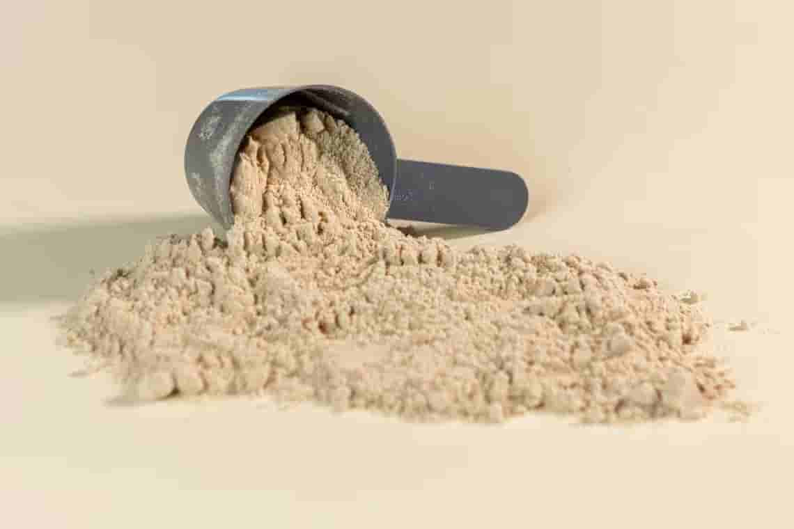 A scoop of light brown protein powder tipped over